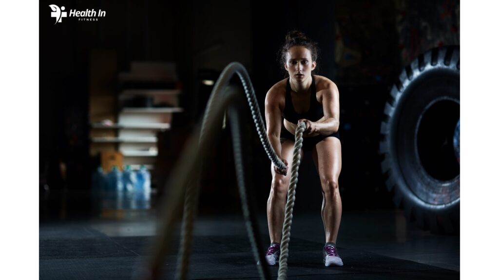 A woman in a fitness gym using battle ropes for an intense workout, showcasing strength and endurance."