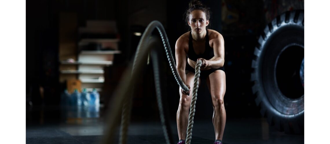 A woman in a fitness gym using battle ropes for an intense workout, showcasing strength and endurance."